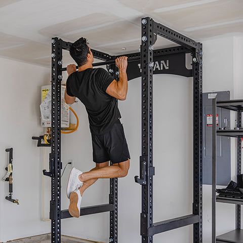 En man gör pull-ups i en kraftig svart träningsställning i ett hemgym.